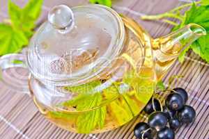 Tea with black currants in glass teapot on bamboo napkin