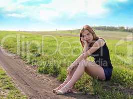 Young sensual smiling blond woman sitting on the grass outdoors