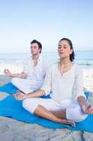 Happy couple doing yoga beside the water