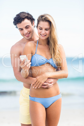 Happy couple in swimsuit looking at mobile phone