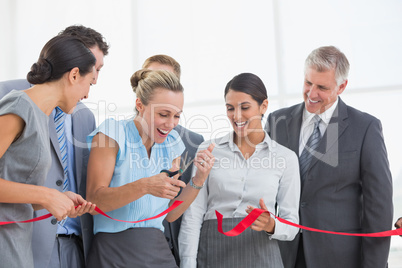 Happy business team cutting red ribbon