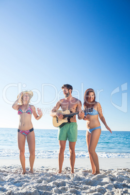 Handsome man playing guitar and his friends dancing