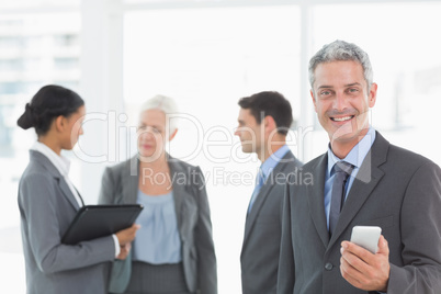 Businessman using a smartphone with colleagues behind in office