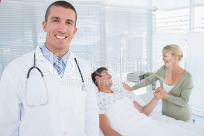 Smiling doctor looking at camera with his patient behind