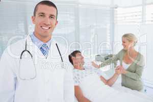 Smiling doctor looking at camera with his patient behind