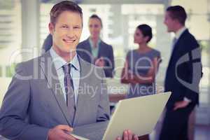 Businessman working on laptop with colleagues behind him