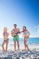 Handsome man playing guitar and his friends dancing