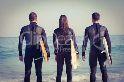 Friends on wetsuits with a surfboard on a sunny day