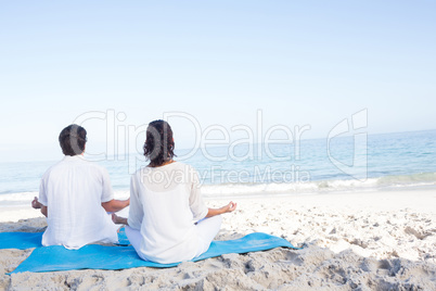 Happy couple doing yoga beside the water