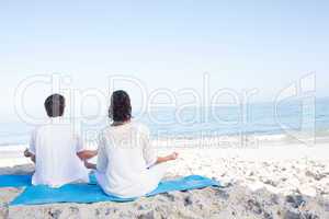 Happy couple doing yoga beside the water
