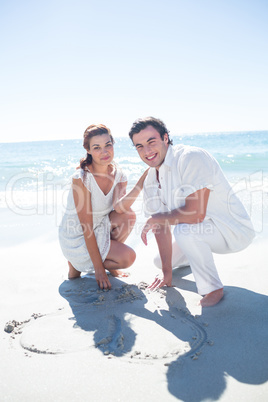 Happy couple drawing heart shape in the sand