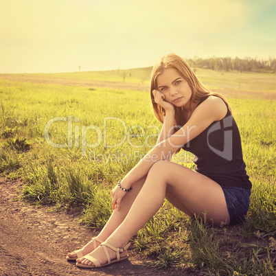 Young sensual smiling blond woman sitting on the grass outdoors