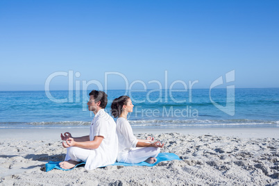 Happy couple doing yoga beside the water