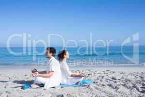 Happy couple doing yoga beside the water