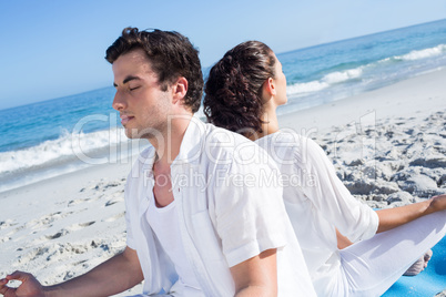 Happy couple doing yoga beside the water