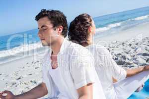 Happy couple doing yoga beside the water