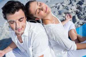 Happy couple doing yoga beside the water