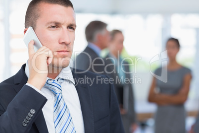 Businessman on the phone with colleagues behind him