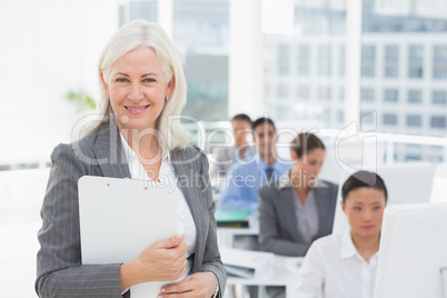 Smiling businesswoman looking at camera while work team using co