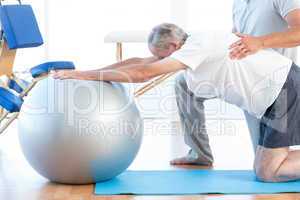 Physiotherapist helping man with exercise ball