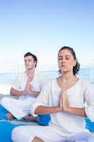 Happy couple doing yoga beside the water