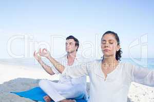 Happy couple doing yoga beside the water