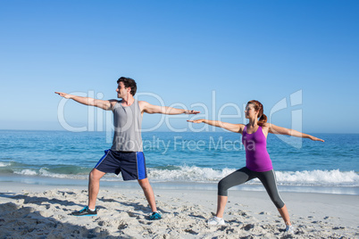 Happy couple doing yoga beside the water