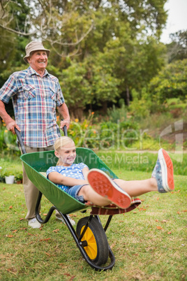 Happy grandfather and his granddaughter with a wheelbarrow