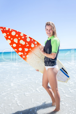 Fit blonde woman standing in the water and holding surfboard