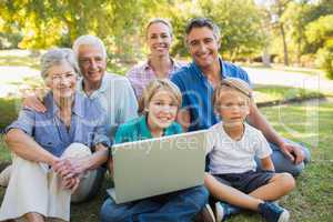Happy family smiling at camera and using laptop in the park