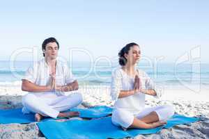 Happy couple doing yoga beside the water