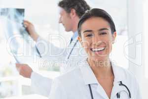 Female doctor smiling at camera while her colleague looking at X