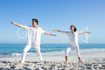 Happy couple doing yoga beside the water