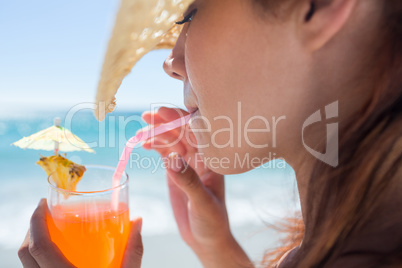 Brunette wearing straw hat and drinking a cocktail