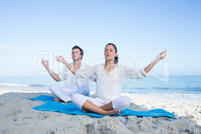 Happy couple doing yoga beside the water