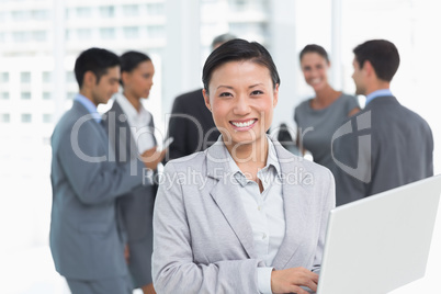 Businesswoman using laptop with colleagues behind