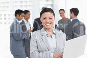 Businesswoman using laptop with colleagues behind