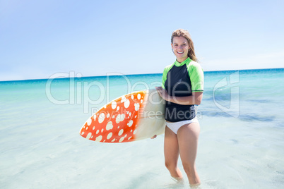 Fit blonde woman standing in the water and holding surfboard