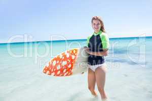 Fit blonde woman standing in the water and holding surfboard