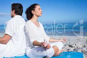 Happy couple doing yoga beside the water