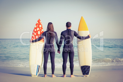 Couple in wetsuits with surfboard on a sunny day