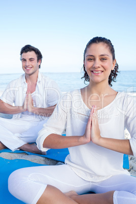 Happy couple doing yoga beside the water