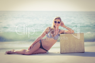 Stylish blonde leaning on suitcase on the beach