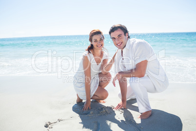 Happy couple drawing heart shape in the sand