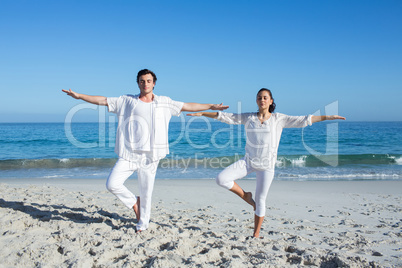 Happy couple doing yoga beside the water