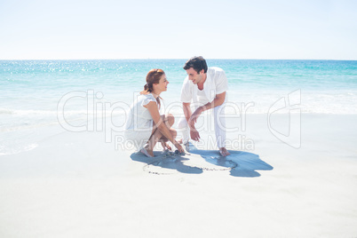 Happy couple drawing heart shape in the sand