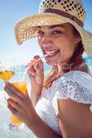 Smiling brunette wearing straw hat and drinking a cocktail