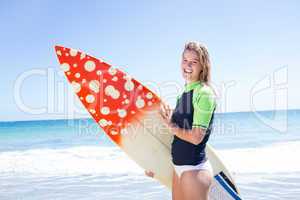 Fit blonde woman standing in the water and holding surfboard
