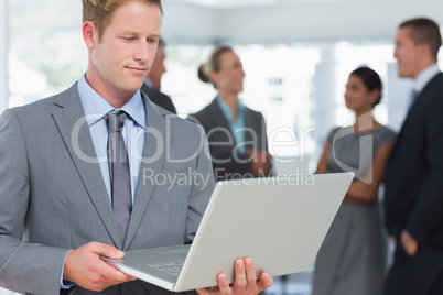 Businessman working on laptop with colleagues behind him