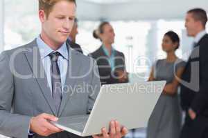 Businessman working on laptop with colleagues behind him